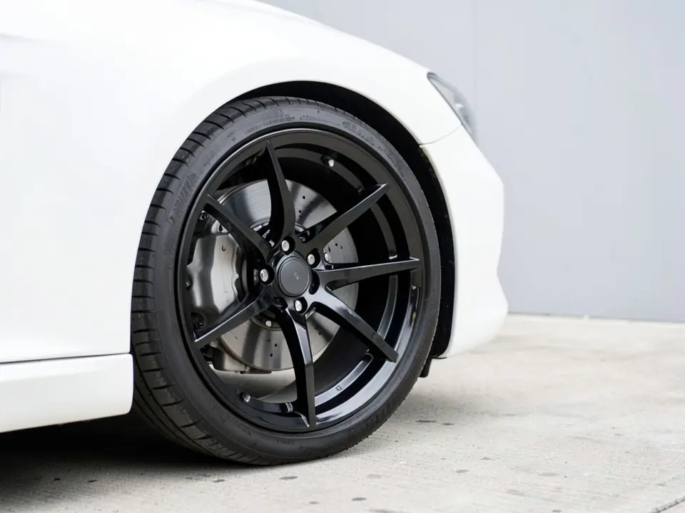 AI-generated sample: front wheel of a white coupe with gloss black thin-spoke wheels and a grey brake caliper