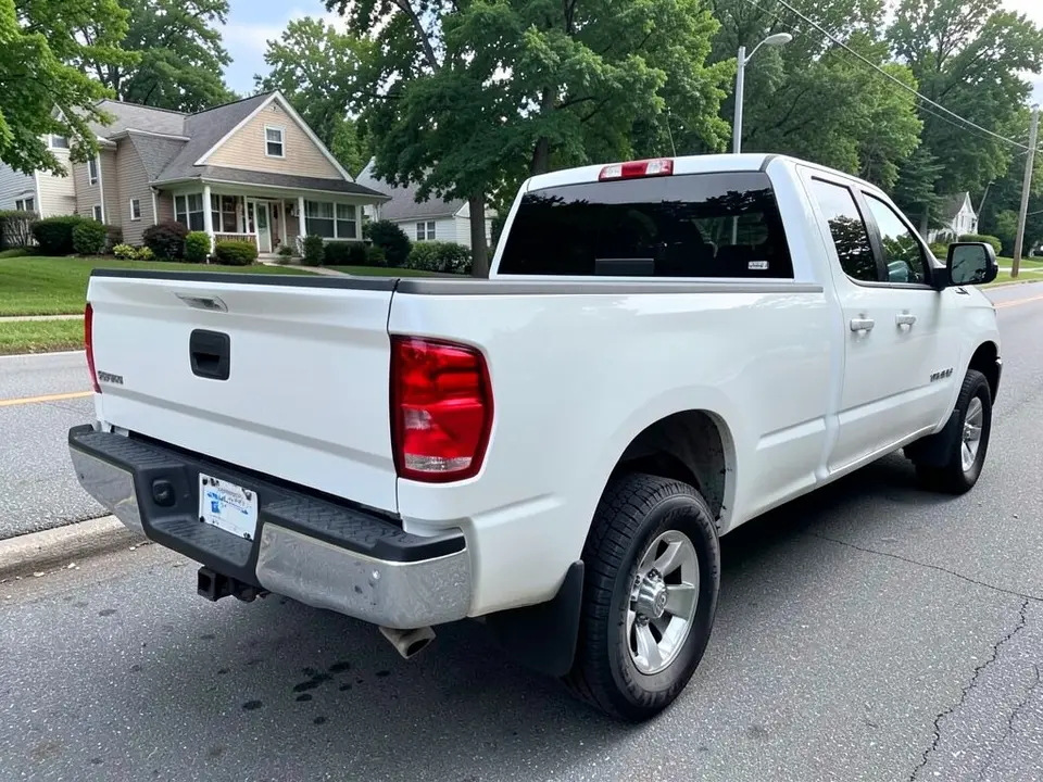AI-drawn sample: a white crew cab pickup truck seen from the rear left corner, showing the tailgate and bed, parked on a suburban street with houses and trees behind